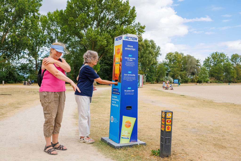 Zwei Frauen cremen sich an einer Sonnencreme-Station des Non-Food-Discounters Action in einem Park ein