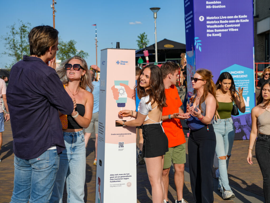 Junge Leute cremen sich an einer Sonnencreme-Station der Krankenkasse Zilveren Kruis mit kostenloser Sonnencreme (LSF 30) bei einem Sommerevent in Nimwegen ein